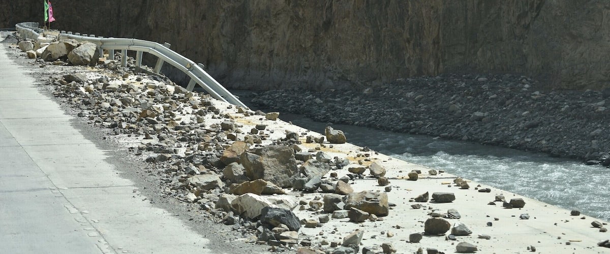 A coastal road with a guardrail, rocky terrain, and a cliff.