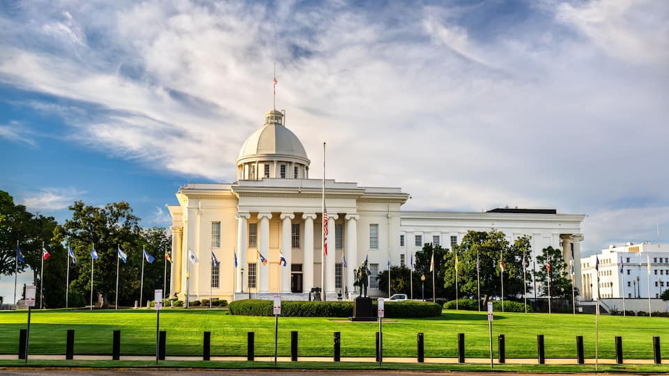 A large white building with a dome and columns, surrounded by a well-maintained lawn and multiple flags.
