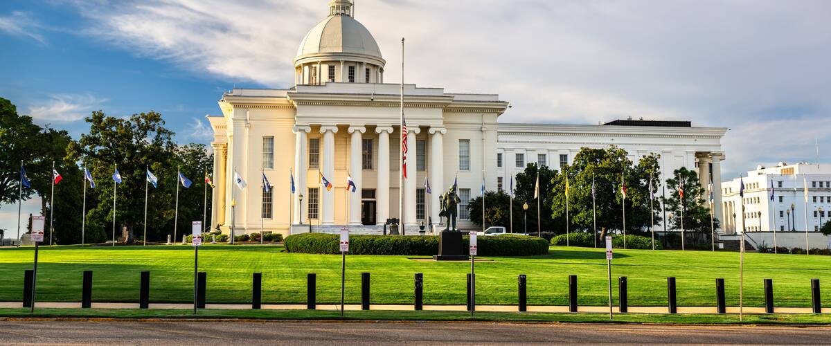 A large white building with a dome and columns, surrounded by a well-maintained lawn and multiple flags.