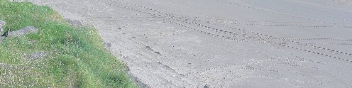 Ein weiter Sandstrand mit sanften Wellen, einem klaren Himmel und fernen Bergen.