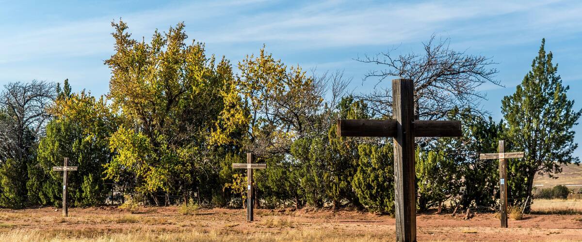 A wooden cross in a field with dry grass and trees in the background.