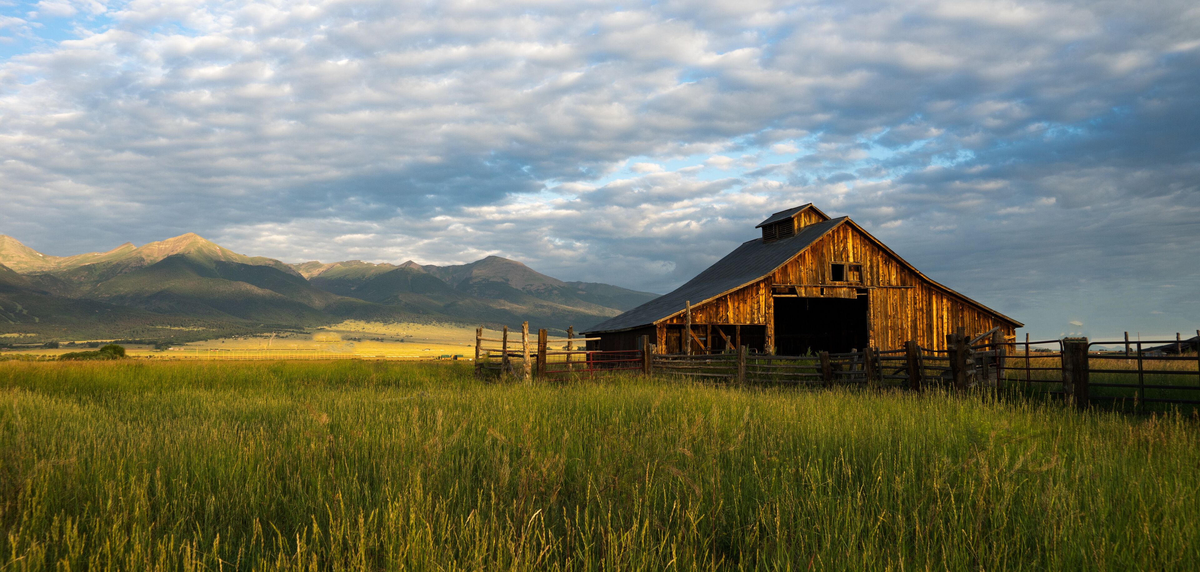 A rustic barn in a grassy field with mountains in the background.