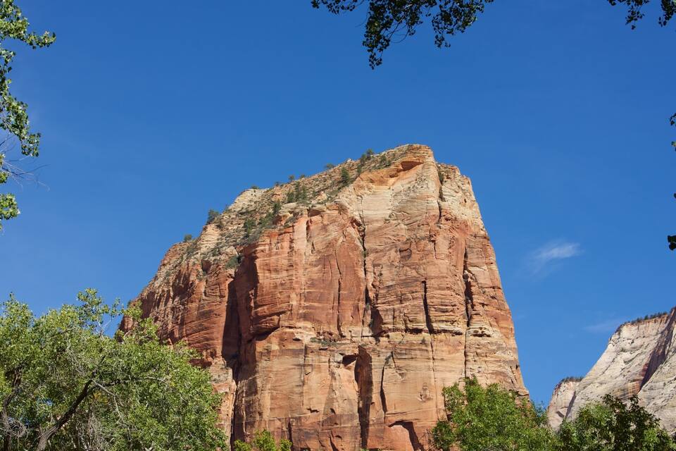 A large red rock formation with trees in the foreground.