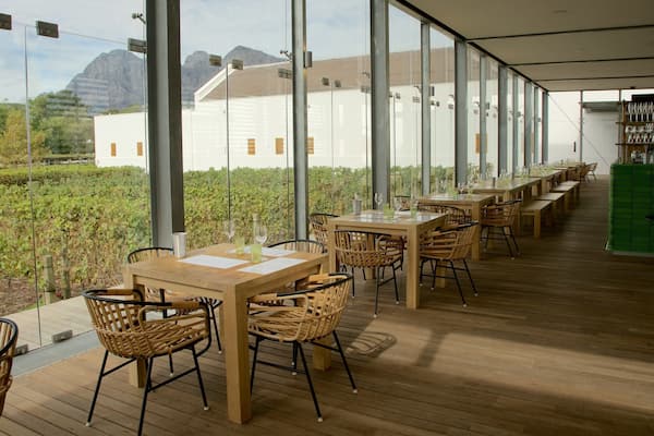 Ein Restaurant mit Außenbestuhlung mit Blick auf einen Weinberg und einen Berg.