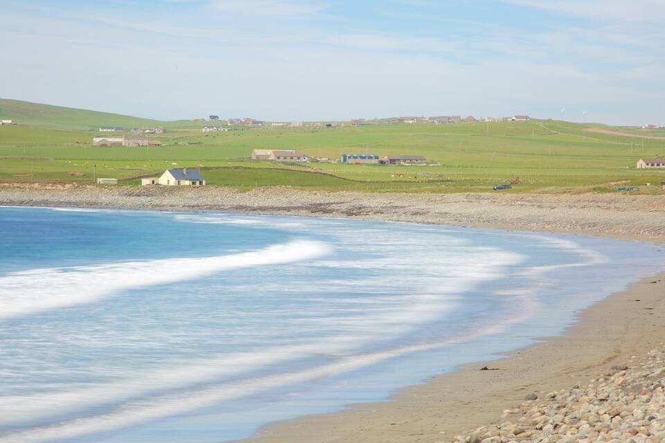 A coastal landscape with a beach, waves, and a distant village.