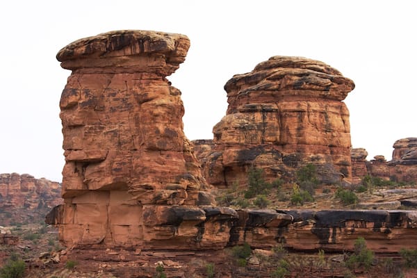Duas formações rochosas imponentes com paisagem desértica ao fundo.