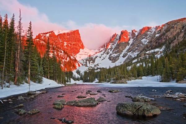 Un paysage de montagne avec une rivière, des sommets enneigés et une forêt dense.
