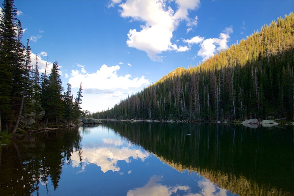A calm lake reflecting the surrounding forest and sky.