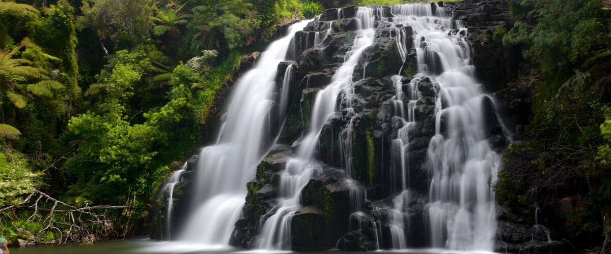 A multi-tiered waterfall surrounded by lush greenery.