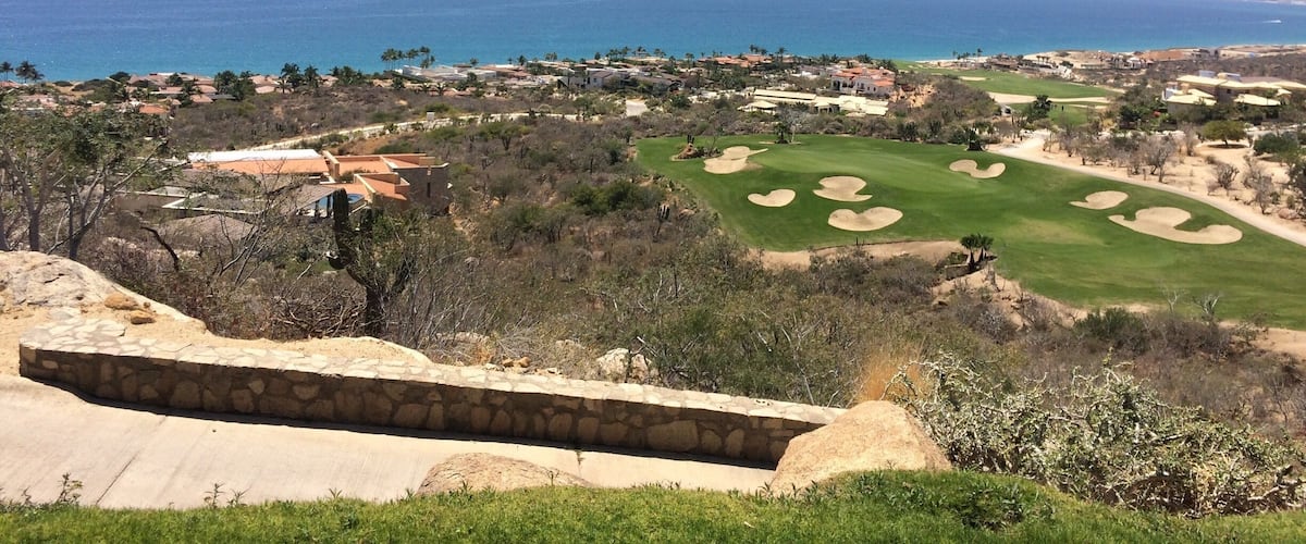 A coastal golf course with a clear view of the ocean and a stone retaining wall in the foreground.