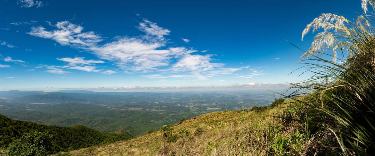 A mountainous landscape with a clear blue sky and scattered clouds.