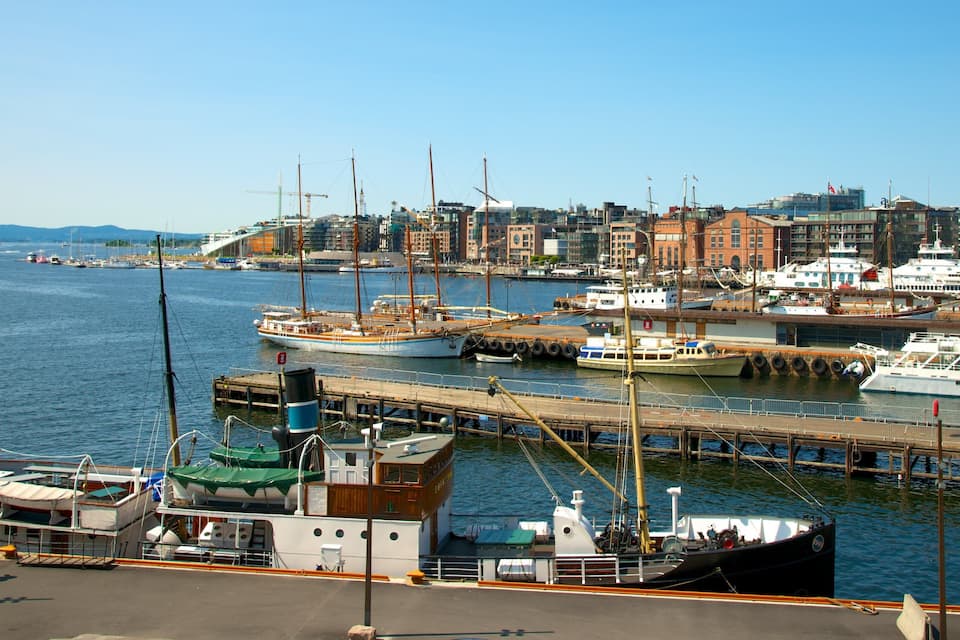 Um porto com vários barcos atracados, um horizonte urbano ao fundo e um céu azul límpido.