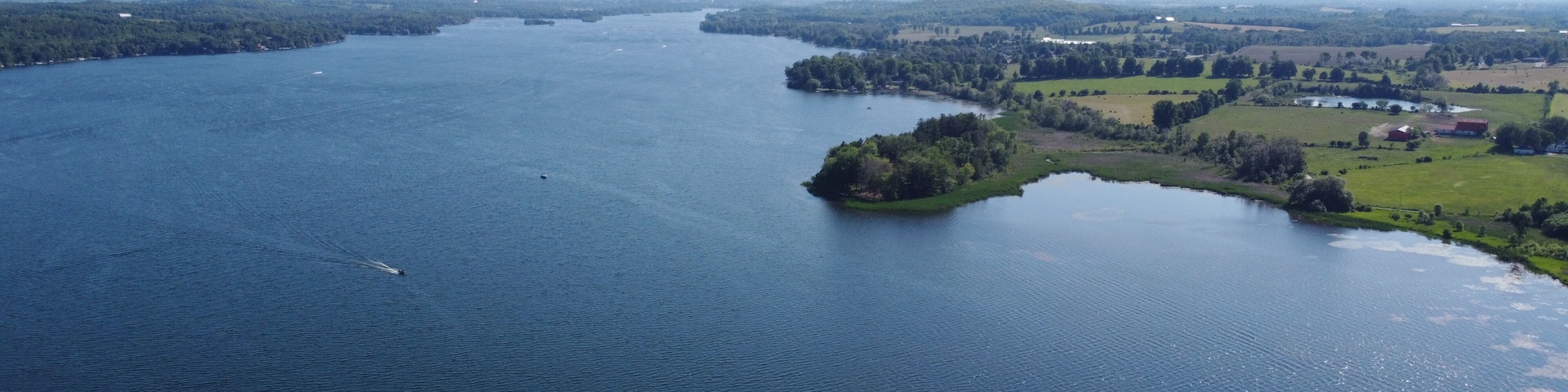 Un extenso cuerpo de agua con una pequeña isla en el centro, rodeado de tierra verde y un cielo despejado.