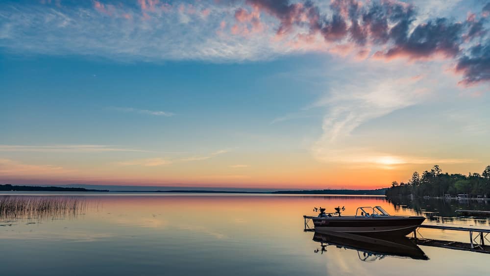 A calm lake at sunset with a boat docked on the right.