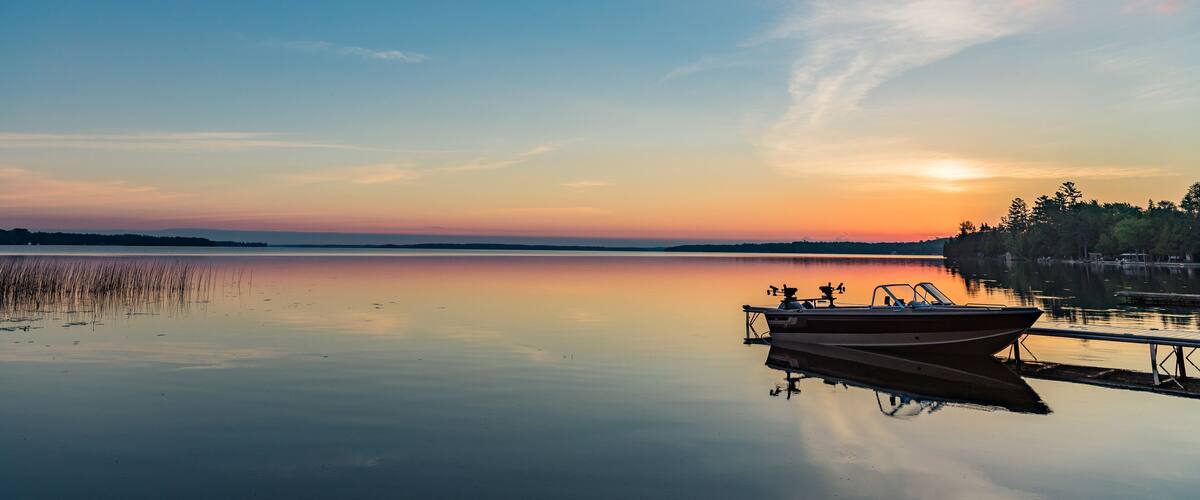A calm lake at sunset with a boat docked on the right.