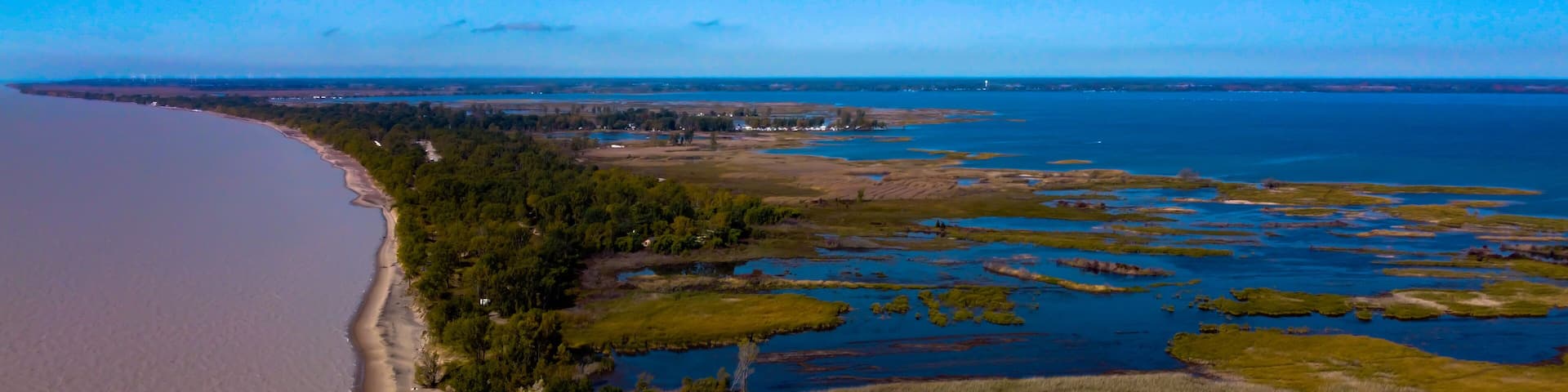 A coastal landscape with a sandy beach, dense forest, and a network of water bodies.