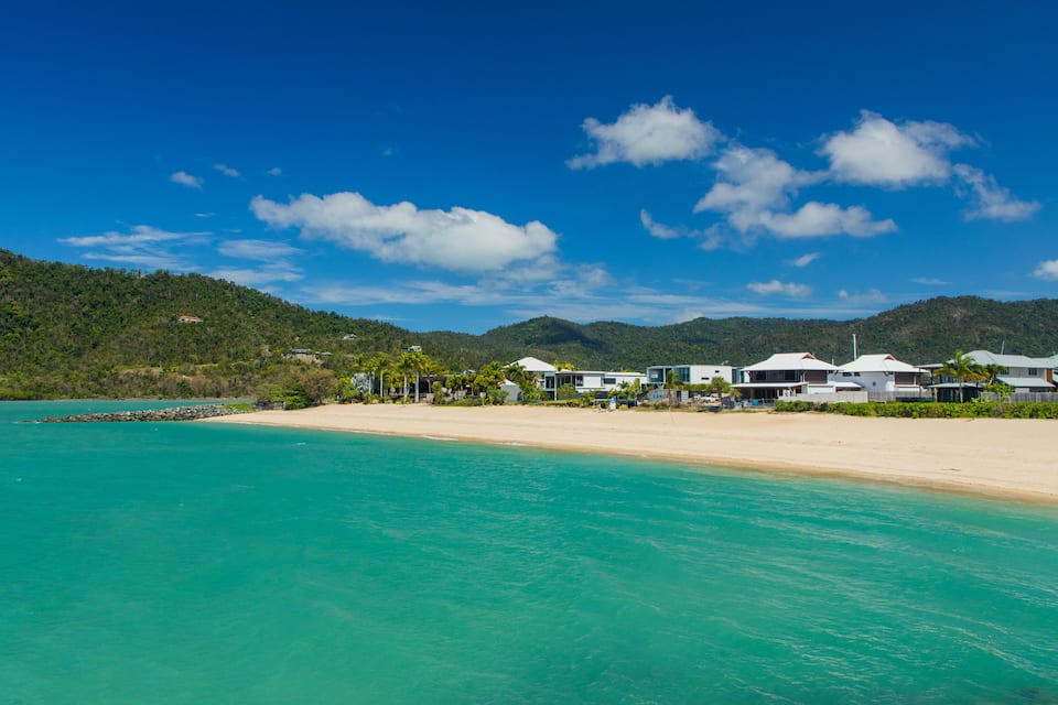 A beach with turquoise water, white sandy shore, and houses with white roofs.