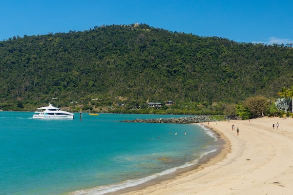 A beach with a boat named 'Cruise Whit Sundays' and a forested hill in the background.