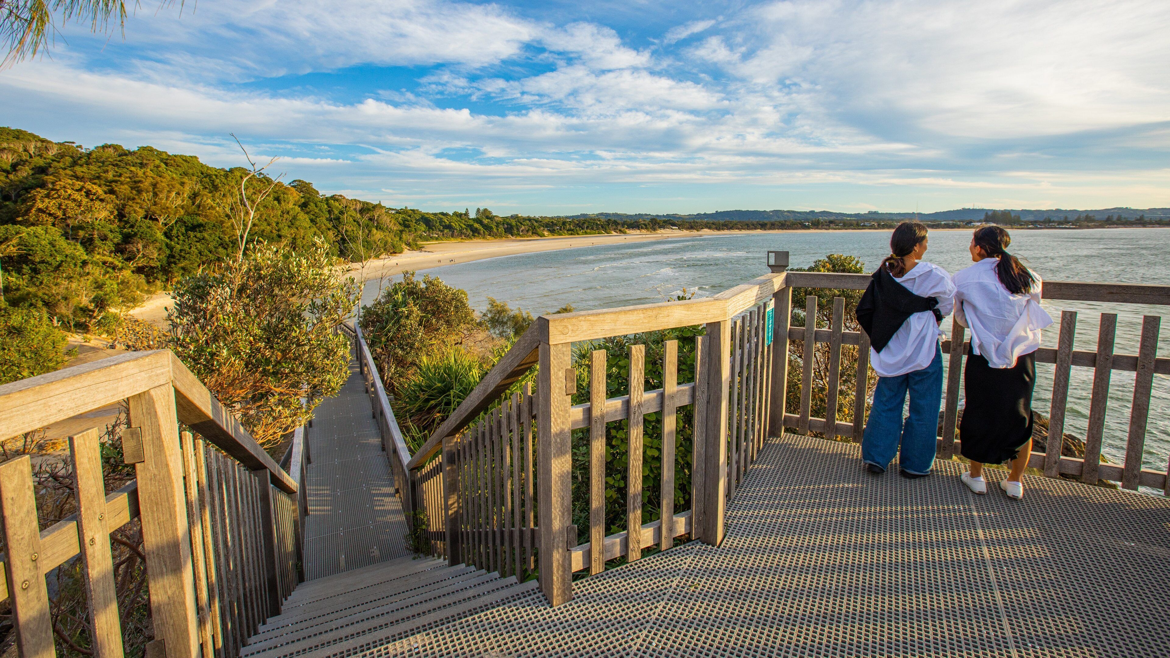 A wooden staircase leading to a viewing platform overlooking a beach and a river.