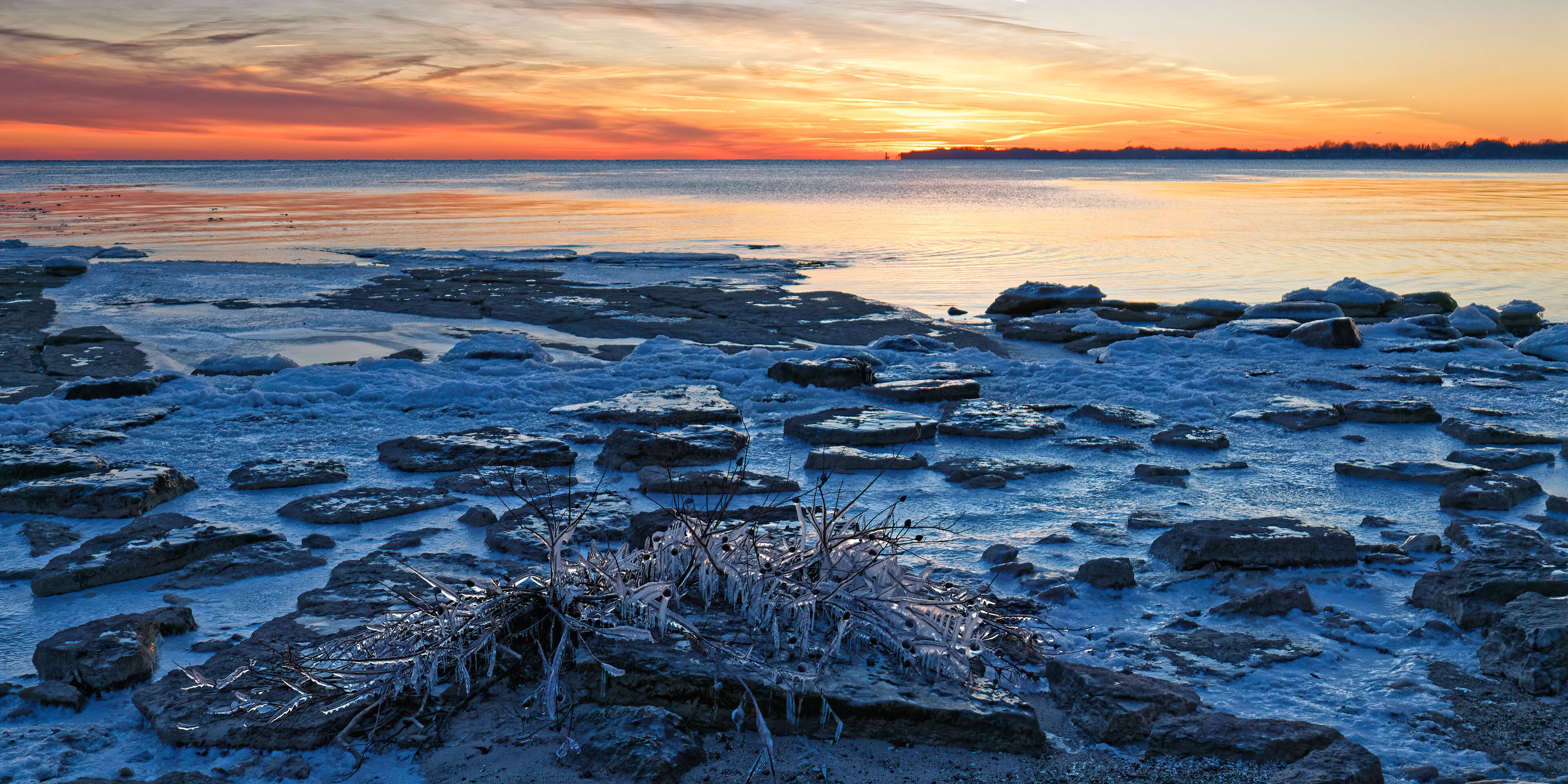 A frozen lake with ice chunks and a sunset in the background.
