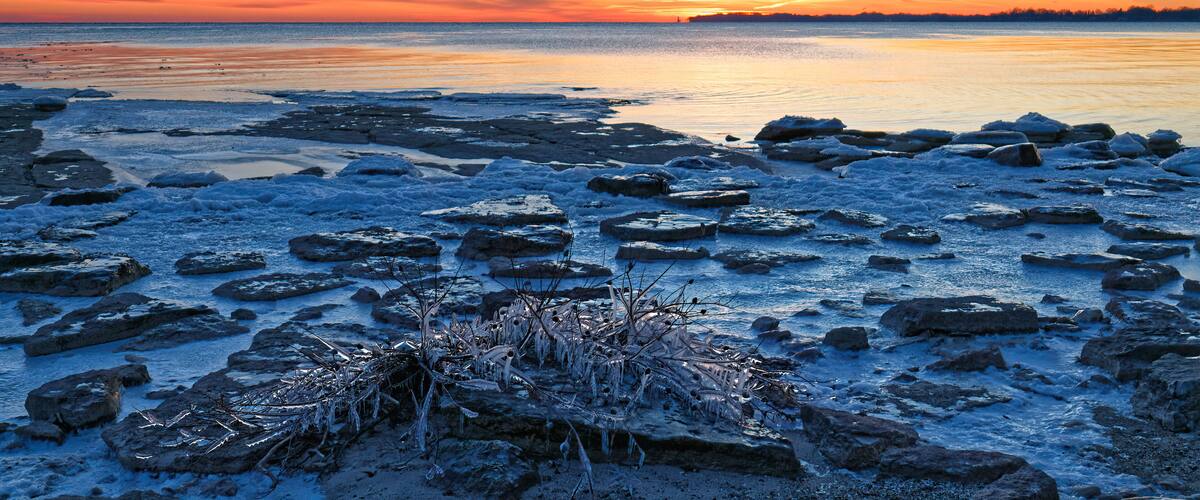 A frozen lake with ice chunks and a sunset in the background.