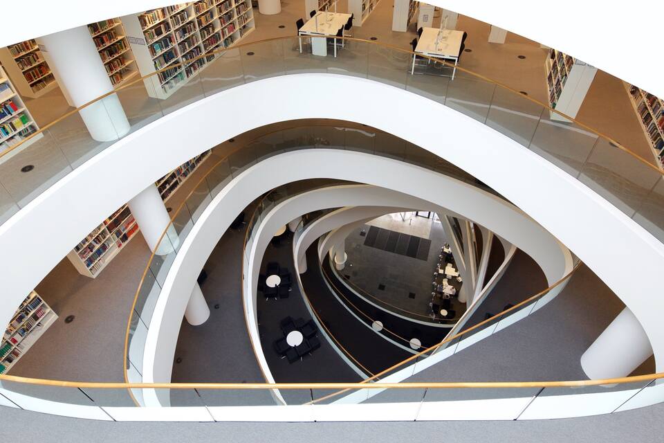 Una biblioteca moderna con varios niveles, barandillas blancas curvas y filas de estanterías.