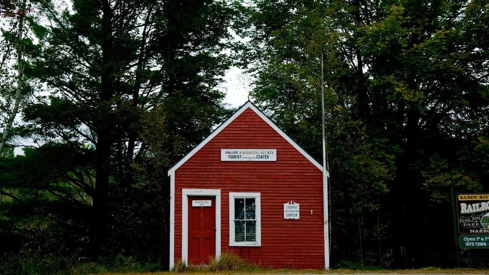 A red historical building labeled as the Phillips Historical Society Tourist Information Center, surrounded by trees.