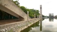 A riverside walkway with a stone embankment, lamp posts, and a tall structure in the background.