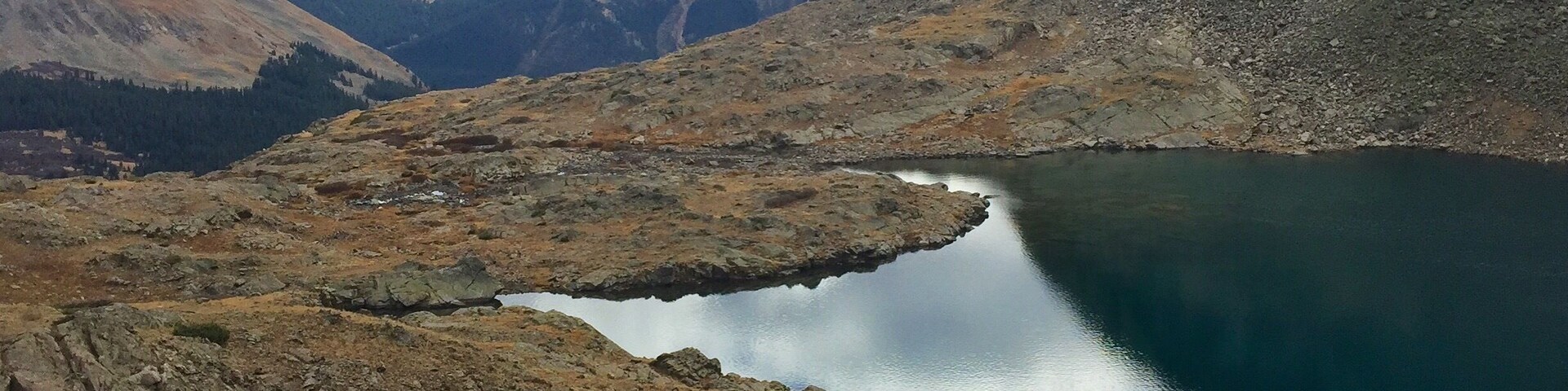 Un paisaje montañoso con un lago rodeado de terreno rocoso y colinas distantes.