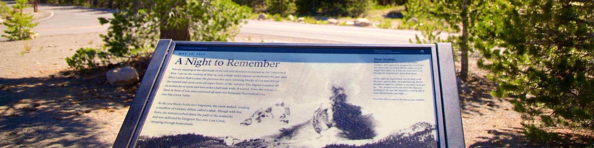 A sign with a historical account of a volcanic eruption, surrounded by trees and a road.