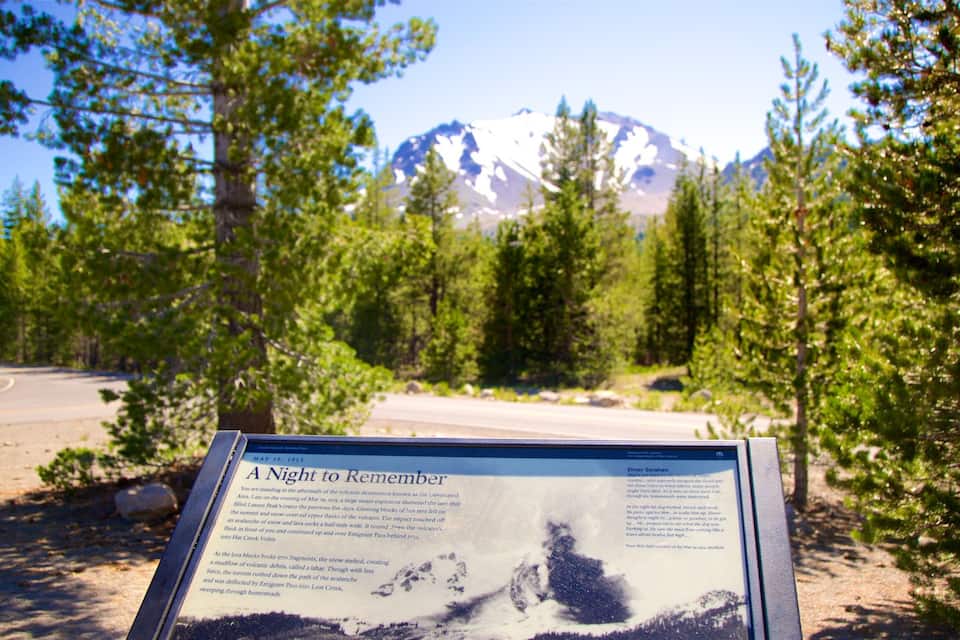 A sign with a historical account of a volcanic eruption, surrounded by trees and a road.