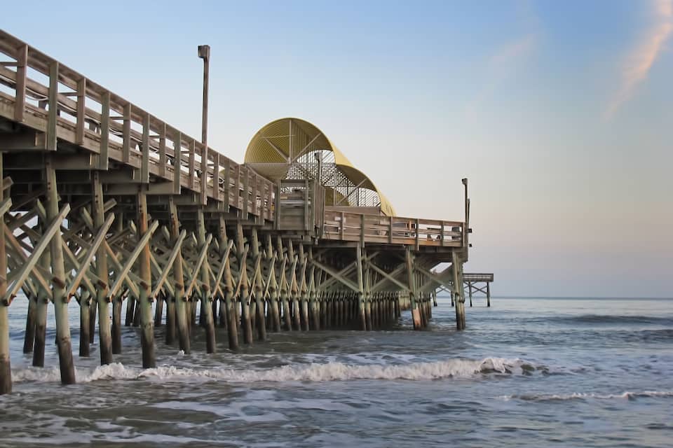A wooden pier extending into the ocean with a large umbrella structure at the end.