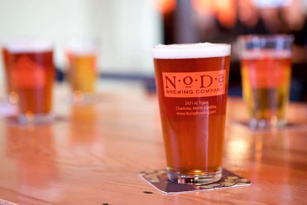 A glass of beer with a label reading "N.O.D. Brewing Company" on a wooden table.
