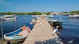 A wooden pier with boats docked on both sides, a clear blue sky, and a distant shoreline with buildings.