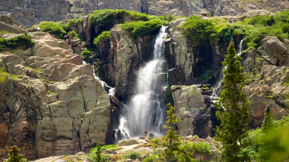 A multi-tiered waterfall surrounded by rocky terrain and lush greenery.
