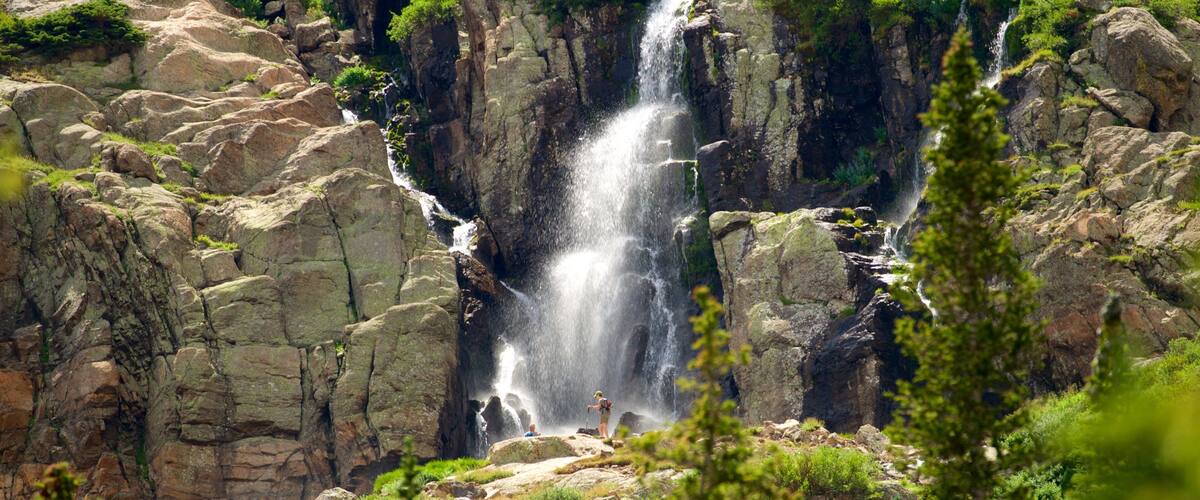 A multi-tiered waterfall surrounded by rocky terrain and lush greenery.