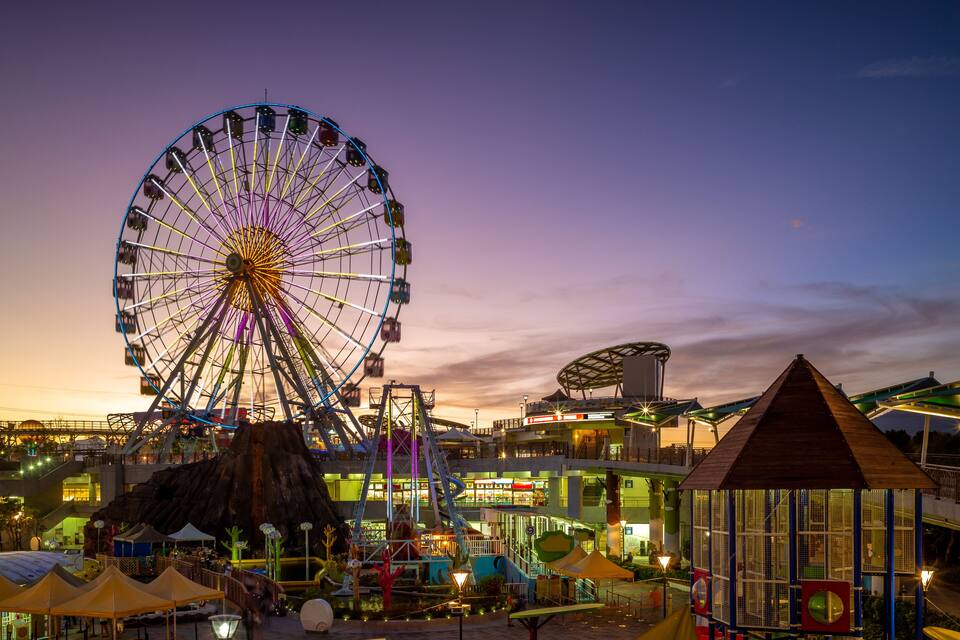 A large Ferris wheel, a water tower, and a wooden structure at dusk.