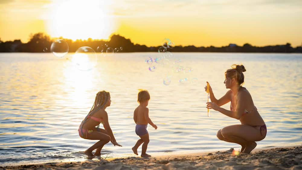 Brother and sister play with their mom blowing bubbles on the lake