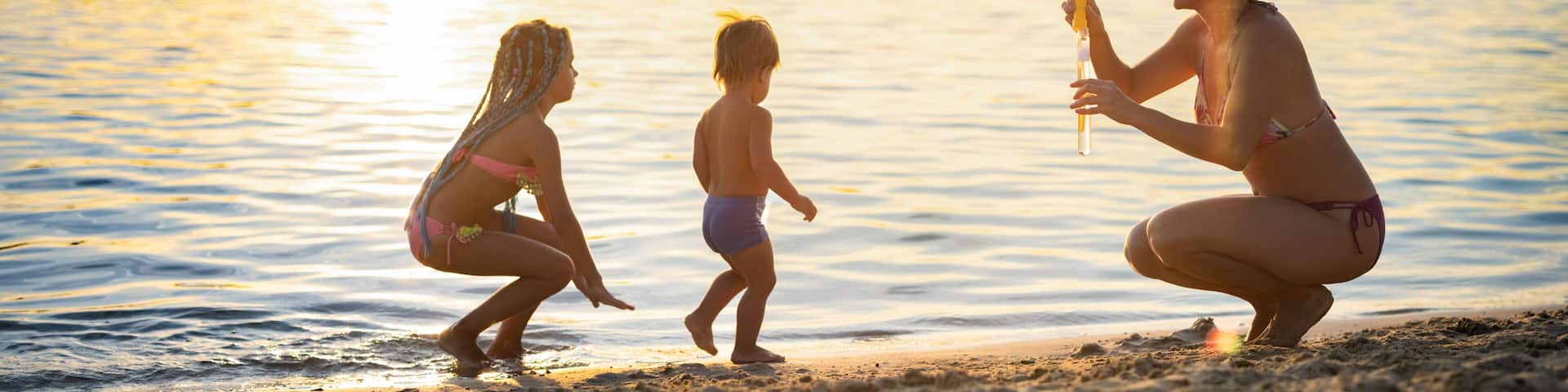 Brother and sister play with their mom blowing bubbles on the lake