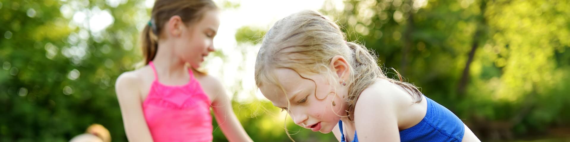 Two little sisters having fun on a sandy lake beach on warm and sunny summer day. Kids playing by the river.