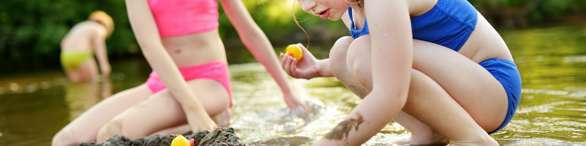 Two little sisters having fun on a sandy lake beach on warm and sunny summer day. Kids playing by the river.