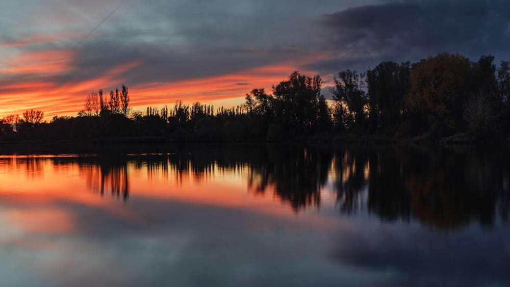 Dramatic weather clouds and sunset light lake panorama with long exposure clouds and trees at the water bank. Südsee in Braunschweig, Germany