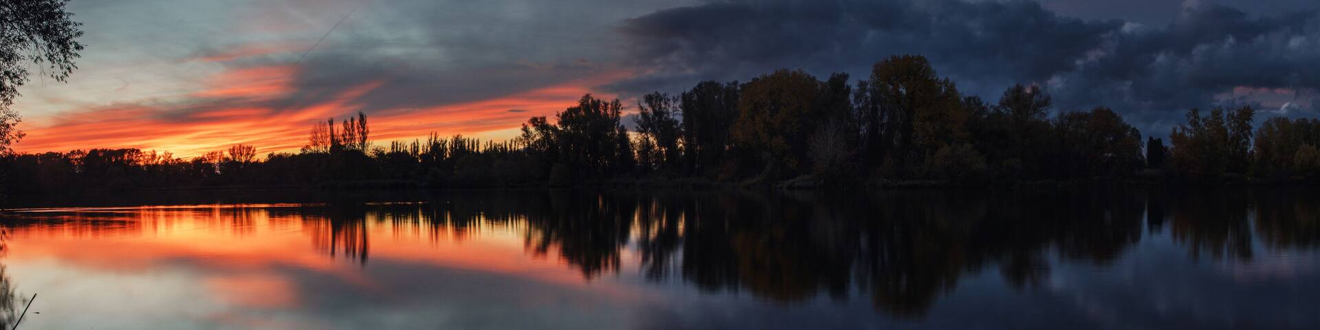 Dramatic weather clouds and sunset light lake panorama with long exposure clouds and trees at the water bank. Südsee in Braunschweig, Germany