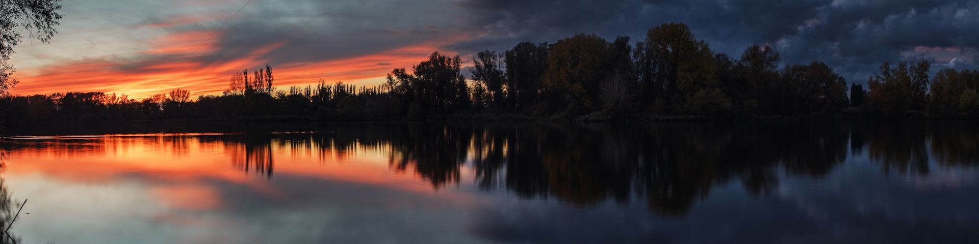 Dramatic weather clouds and sunset light lake panorama with long exposure clouds and trees at the water bank. Südsee in Braunschweig, Germany