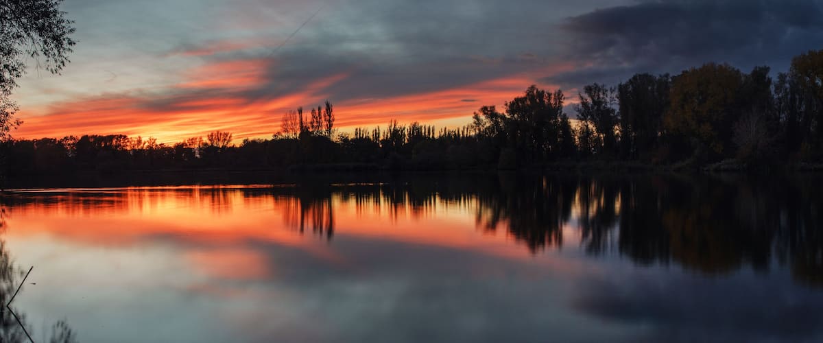 A sunset over a calm lake with trees reflecting the sky.