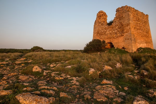 A large, ancient stone structure with a collapsed upper section, surrounded by grassy terrain and scattered rocks.