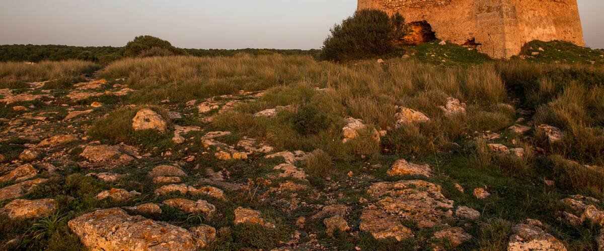 A large, ancient stone structure with a collapsed upper section, surrounded by grassy terrain and scattered rocks.