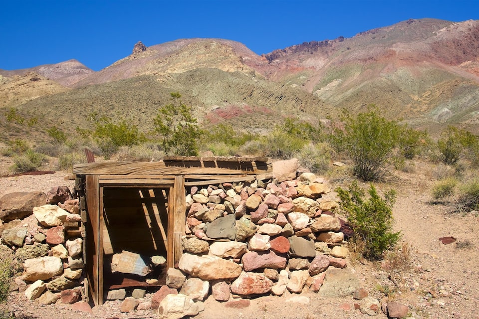 A rustic stone structure with a wooden door in a desert landscape with mountains in the background.