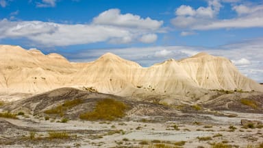 A desert landscape with rolling sand dunes and pale-colored rock formations under a partly cloudy sky.