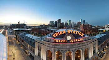 union station panorama with neon travel by train sign and clock and Denver city skyline in the background at sunrise